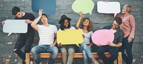 A group of young people hold empty colourful paper speech bubbles, symbolizing face-to-face verbal conversation and real-world communication opposite to online texting.