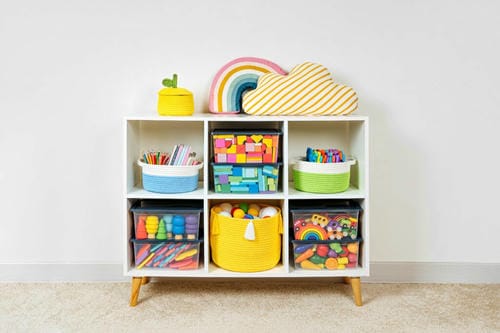 A six-grid open shelving unit uses woven fabric baskets and transparent plastic boxes to categorize crayons, building blocks and small toys, achieving systematic, clutter-free toy storage.