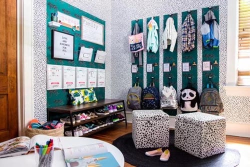 A styled entry nook features wall-mounted coat pegs for jackets, a shoe bench for footwear, labeled backpack hooks, wall file organizers for papers, and compact storage stools, creating a tidy dedicated spot for daily family items.