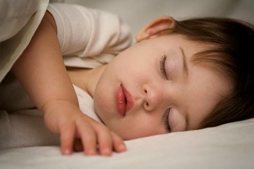 The young child lies peacefully in bed with eyes closed, falling into deep sleep after enjoying late-night snacks.