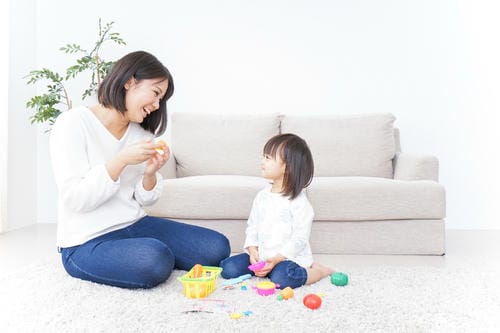 A Japanese mother sits on the fluffy living-room carpet, smiling and playing colorful pretend food toys with her little girl, enjoying warm interactive parent-child playtime at home.